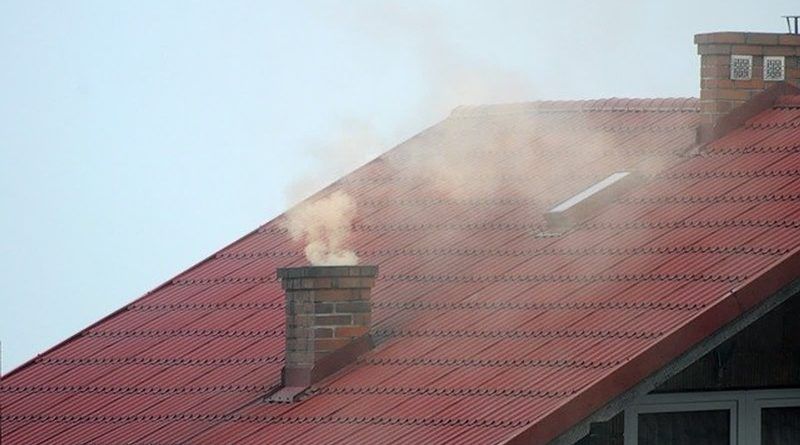 Widok komina na dachu budynku emitującego gęsty dym.